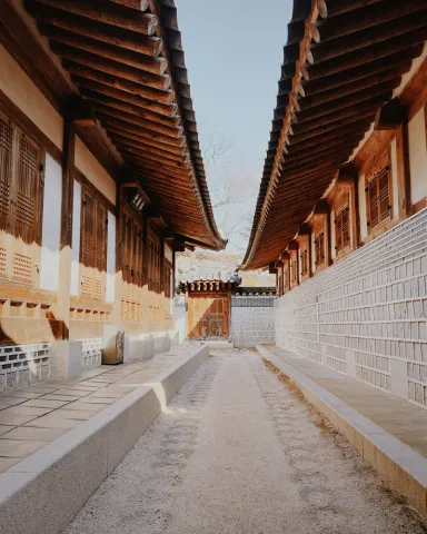Narrow stone alleyway lined with traditional hanok houses in a historic Korean village, featuring wooden doors and tiled roofs