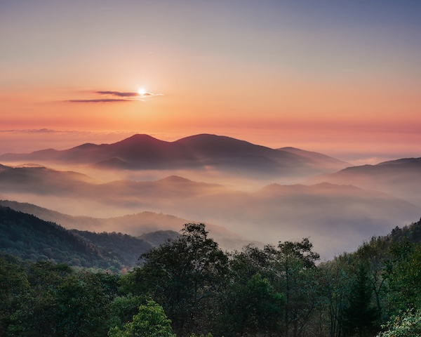 The sun rises over the majestic Smoky Mountains in Asheville, North Carolina, casting a warm glow across the landscape.