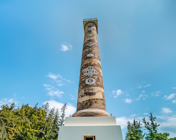 The 125-foot-tall Astoria Column Tower standing tall against a clear blue sky, surrounded by lush greenery.