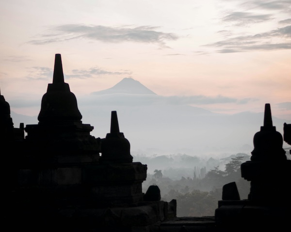 The silhouette of a mountain rises behind Borobudur Temple, creating a stunning backdrop in Indonesia.