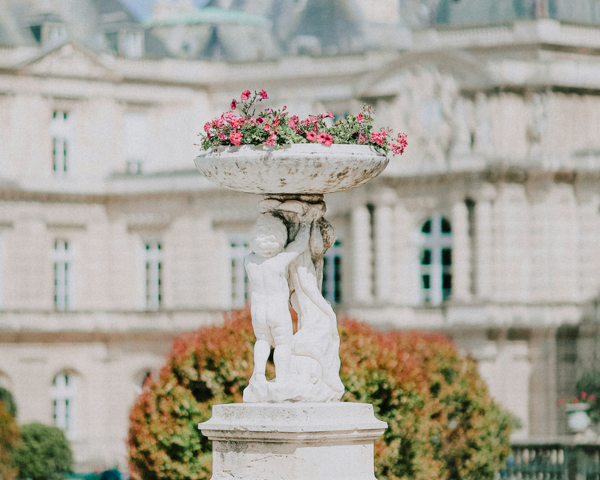 A statue of a woman surrounded by flowers in a fountain, set against the backdrop of Paris.