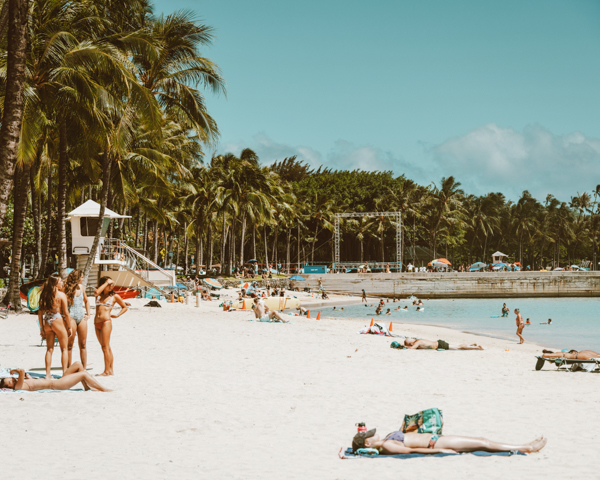  A group of people relaxing and sunbathing on a sandy beach under a clear blue sky.