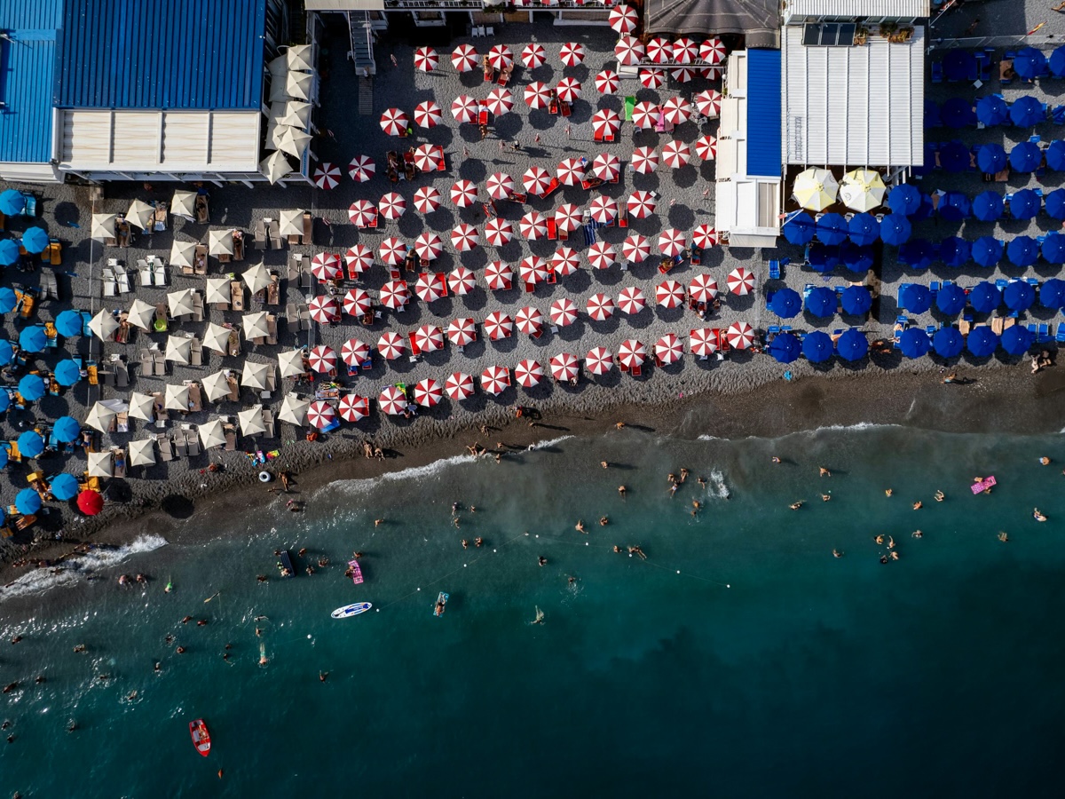 Aerial view of vibrant, colourful umbrellas dotting the sandy beach along the Amalfi Coast in Italy, with turquoise waters gently lapping the shore.