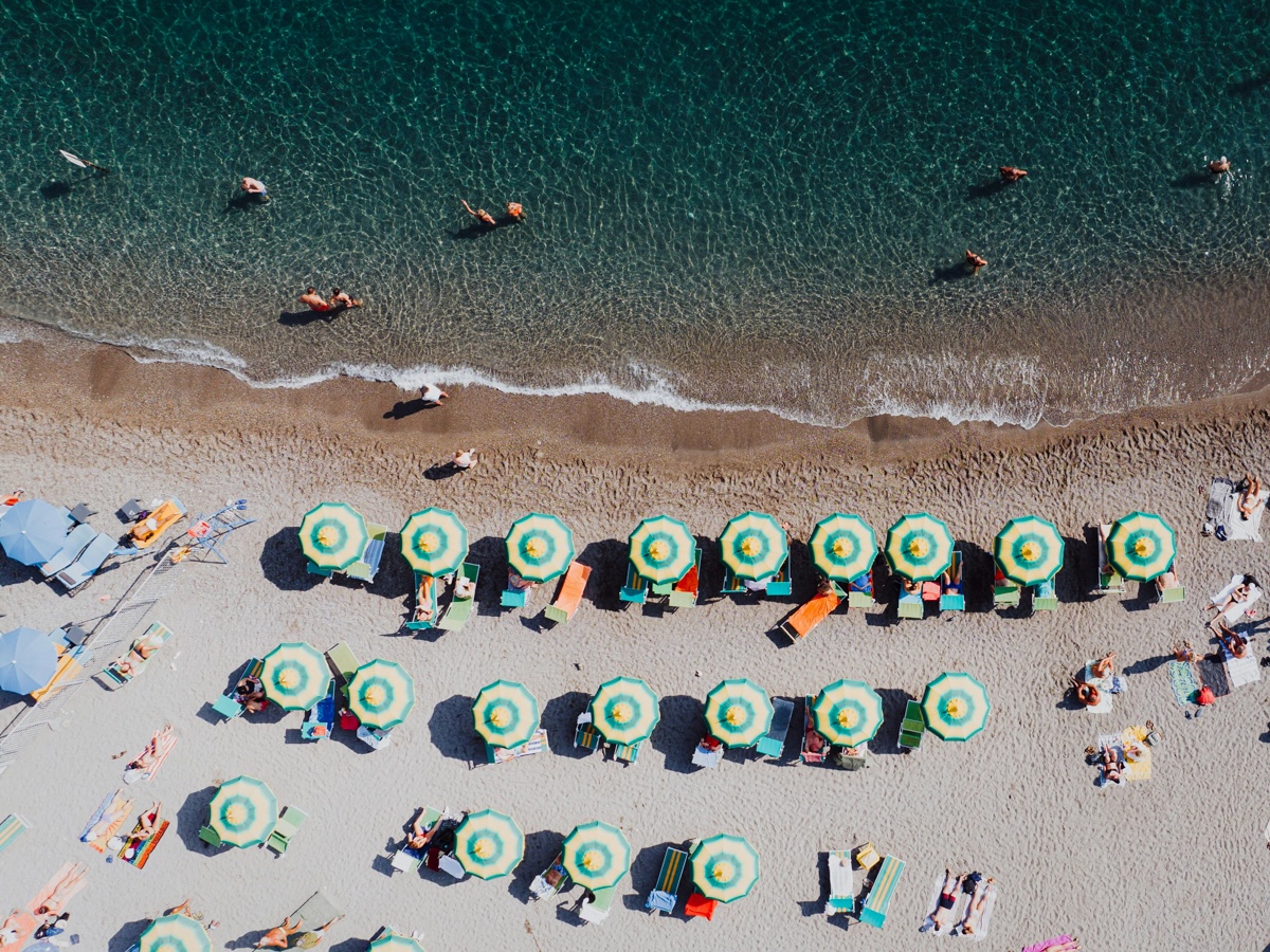 A vibrant beach on the Amalfi Coast, Italy, dotted with colourful umbrellas and sunbeds, with turquoise waters.