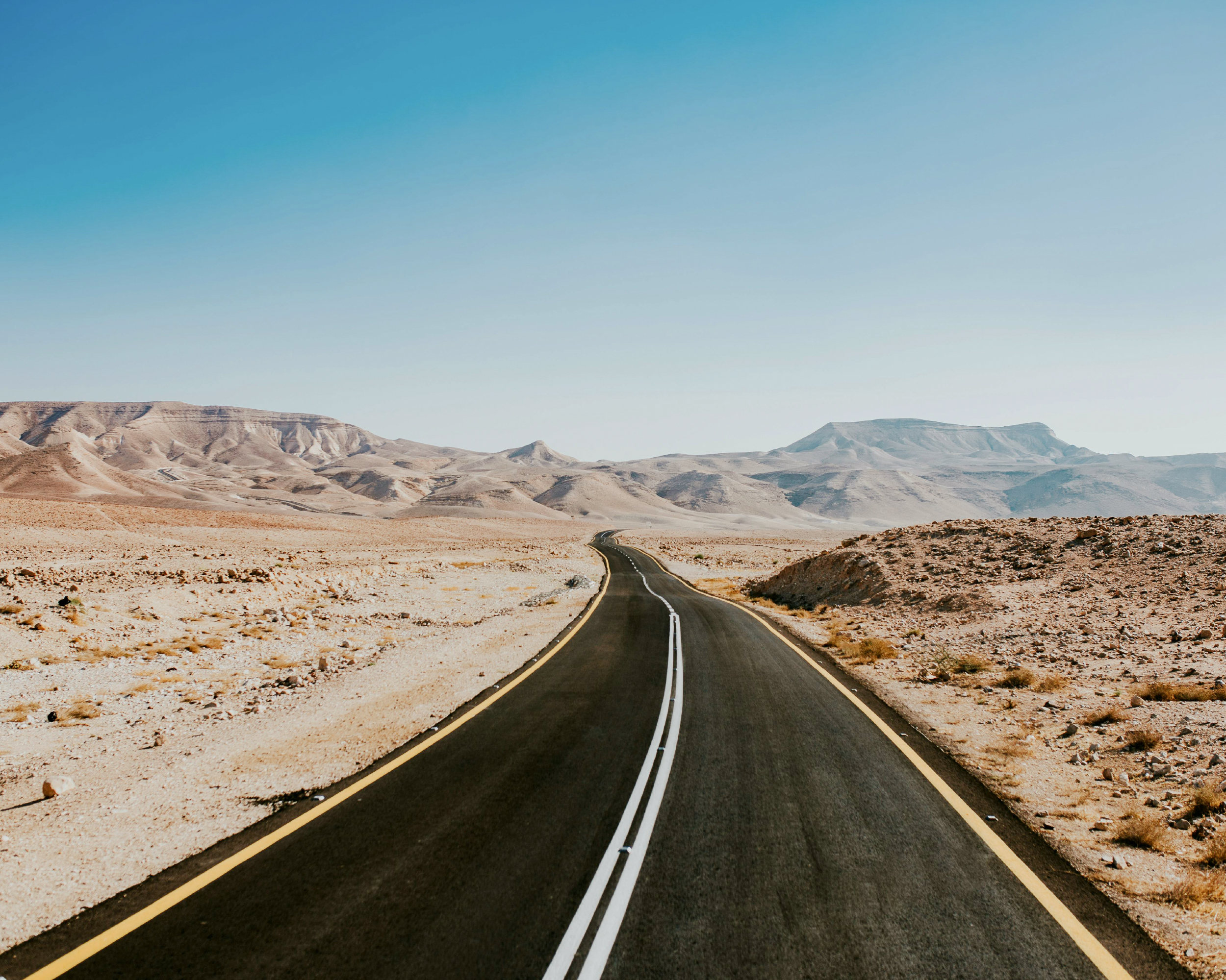 Straight road through a desert landscape under clear blue sky, ideal for car rental road trips.