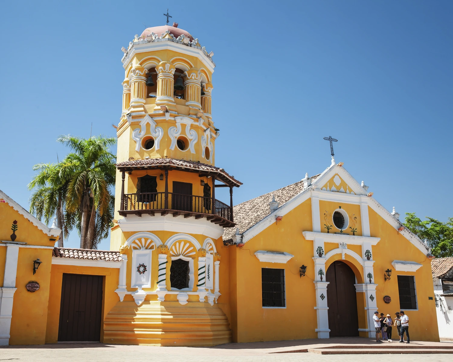 Front view of a bright yellow colonial church with a bell tower in Santa Cruz de Mompox, Colombia, under a clear blue sky.