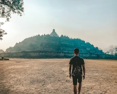 A man strolls towards the majestic Borobudur Temple in Indonesia, surrounded by lush greenery and ancient architecture.